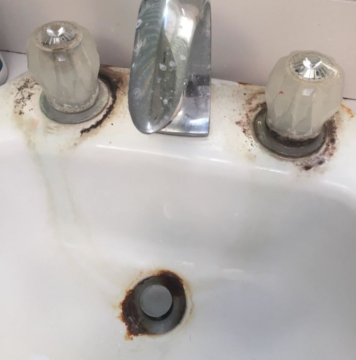 A bathroom sink showing signs of rust and grime around the faucet and drain, highlighting the need for cleaning or replacement.