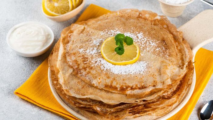 A plate stacked high with thin pancakes.