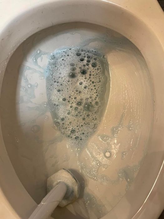 A toilet bowl with foamy cleaning solution being scrubbed