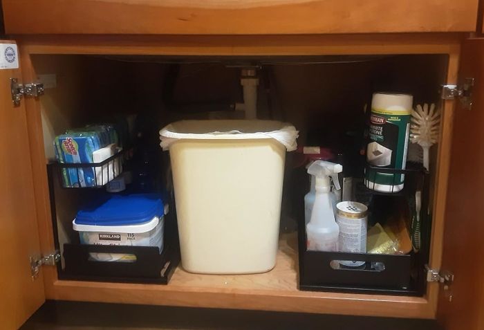 Neatly arranged under-sink storage, with cleaning supplies, a trash bin, and hygiene products tucked into pull-out drawers