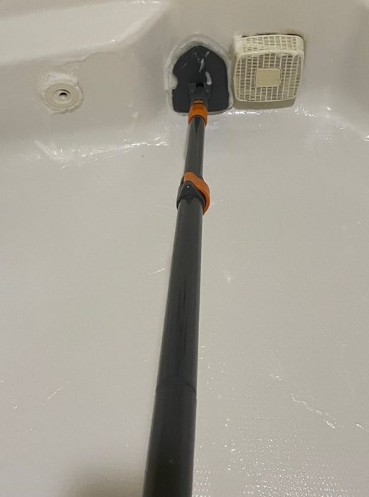 A cleaning tool stretching towards a ventilation fan in a bathtub, showcasing how to effortlessly clean hard-to-reach ceiling fixtures