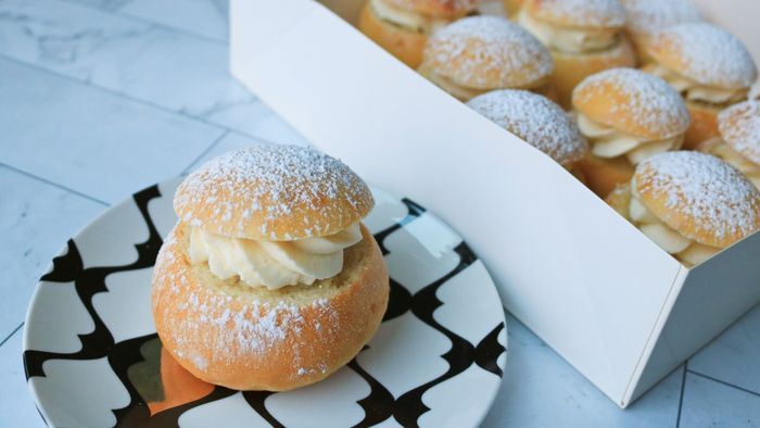 A plate of semla buns alongside a box filled with more semlor buns.