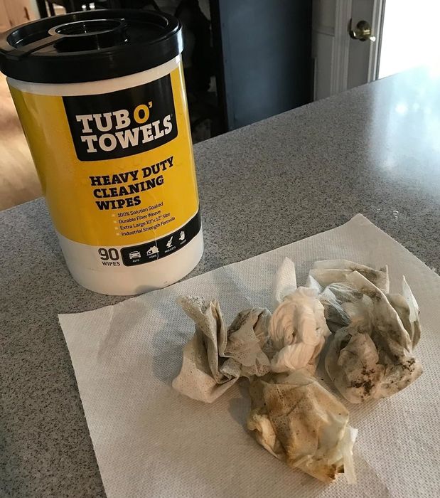 A Tub O' Towels container of heavy-duty cleaning wipes, sitting next to used and dirty wipes on a paper towel on the countertop