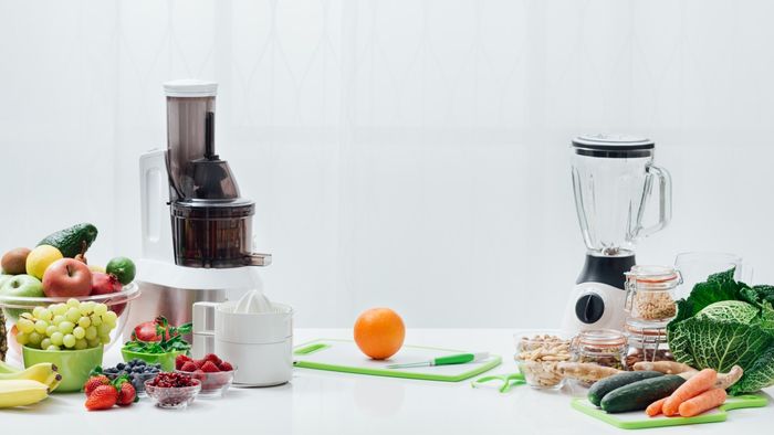 A juicer and a blender placed on a countertop next to fresh fruits and vegetables