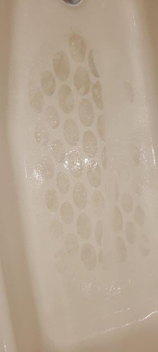 A close-up of an old bathtub, with worn non-slip adhesive dots on its surface