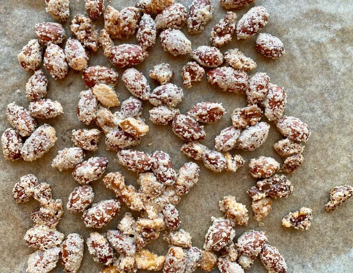 Sugared nuts spread out on a sheet of parchment paper.