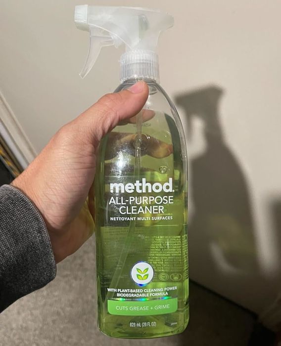 A hand holds a bottle of Method All-Purpose Cleaner, showcasing its plant-based cleaning power and eco-friendly formula. The label highlights its ability to cut through grease and grime.