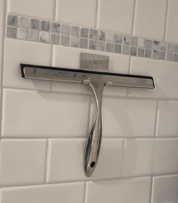 A shower squeegee with a sleek metallic handle, mounted on a tiled bathroom wall