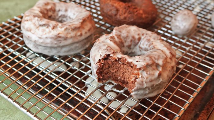 A chocolate doughnut with a bite taken out, resting on a cooling rack.