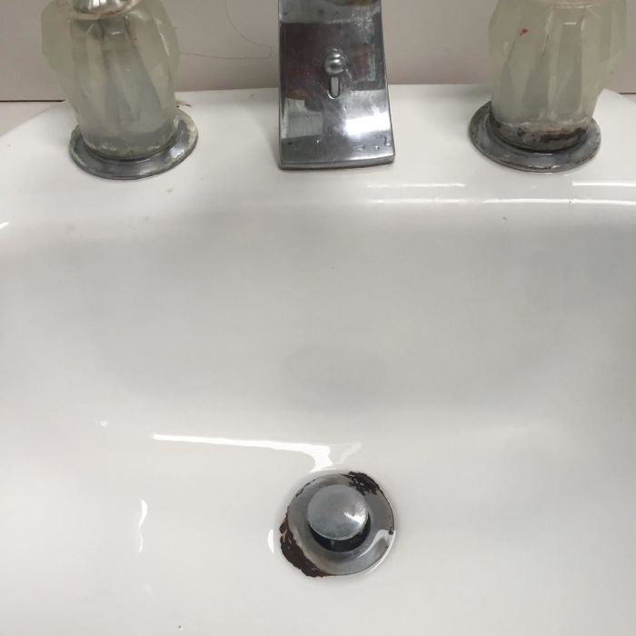 A white sink with two faucet handles and a central spout, showing visible wear around the drain.
