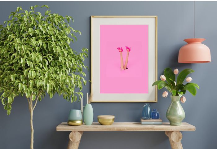 The pink digital print featuring a girl with pink heels, framed and hanging on a wall.