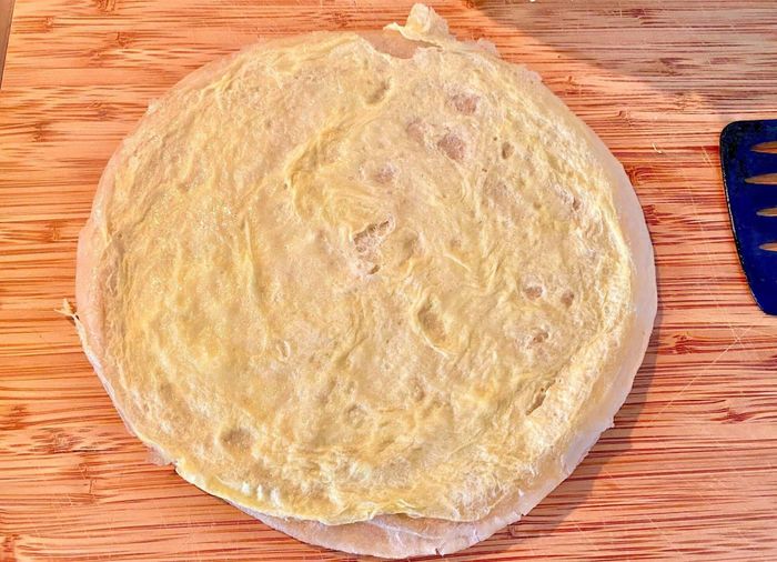 The tortilla is flipped from the pan onto a cutting board, with the thin egg layer facing upwards.