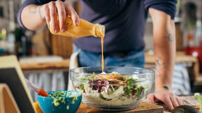 A person drizzling salad dressing over a fresh salad