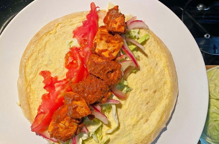 A layered chicken frankie featuring masala-spiced chicken chunks, sliced tomatoes, cabbage, and pickled onions.