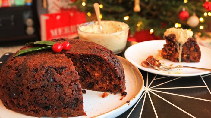 A Christmas pudding served alongside a slice, accompanied by rich brandy butter.
