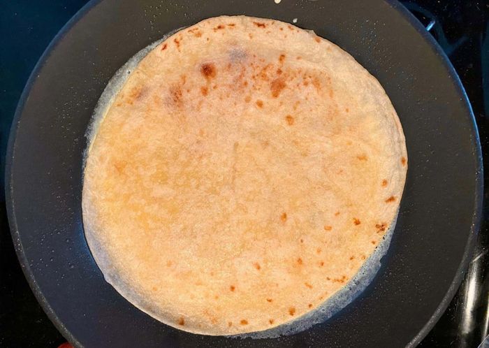 The tortilla is placed in the frying pan, then gently added on top of a thin omelette layer.