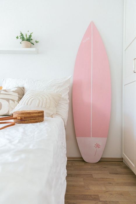 A surfboard placed beside a pristine white bed.