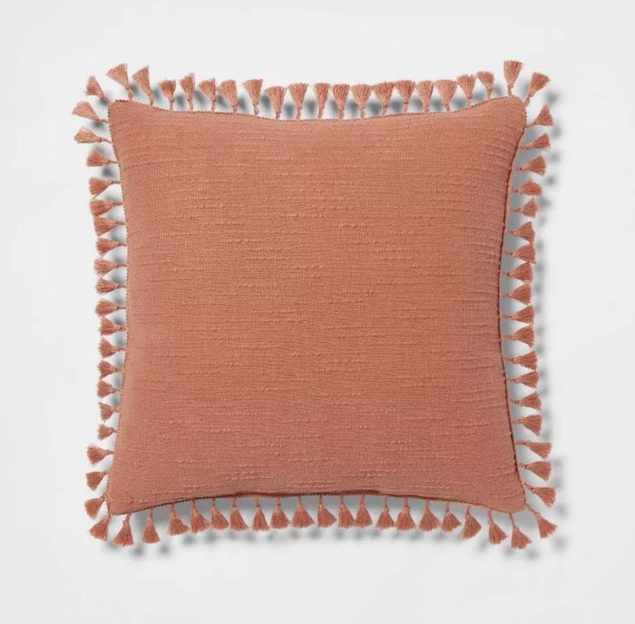 An orange throw pillow with tassels.