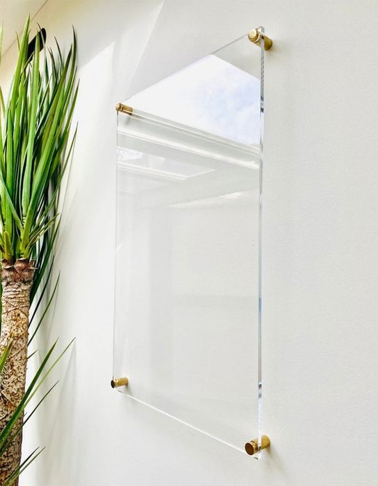 A square transparent whiteboard with four gold knobs mounted on a wall