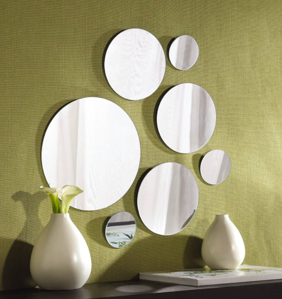 A collection of seven large and small circular mirrors mounted on a green wall above a table