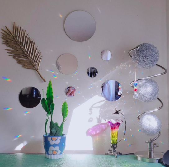 A reviewer demonstrates their circular mirror arrangement placed above a dresser, paired with a small plant pot and sparkly disco ornaments