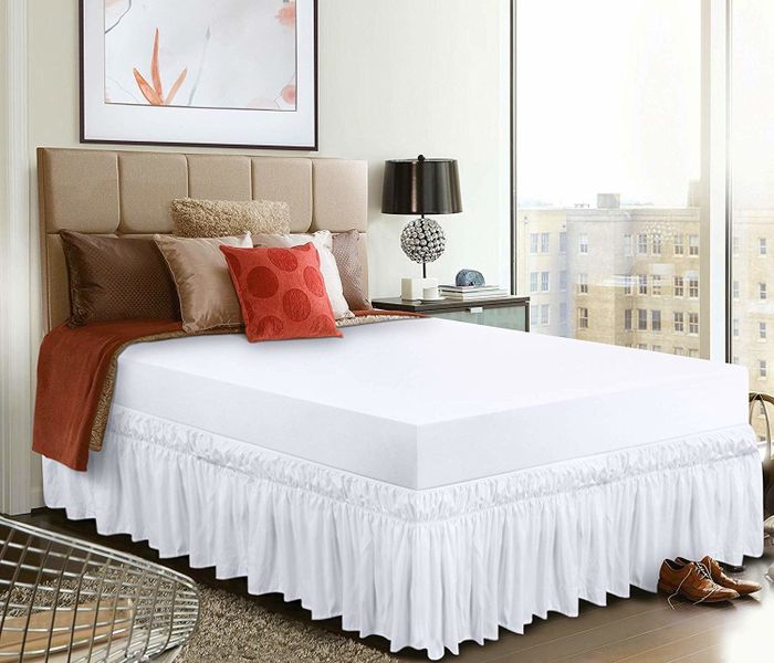A bed adorned with a white dust ruffle.