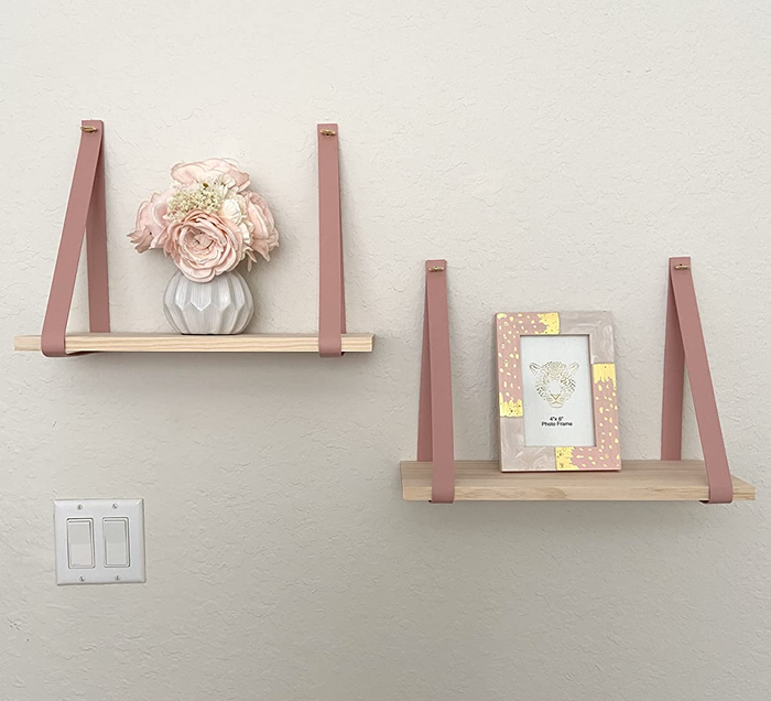 A pair of wooden shelves supported by soft pink leather straps