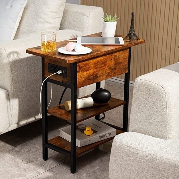 A wooden side table with shelving, equipped with a charging station. The table is adorned with decor items including a tablet, cups, and a small Eiffel Tower model.