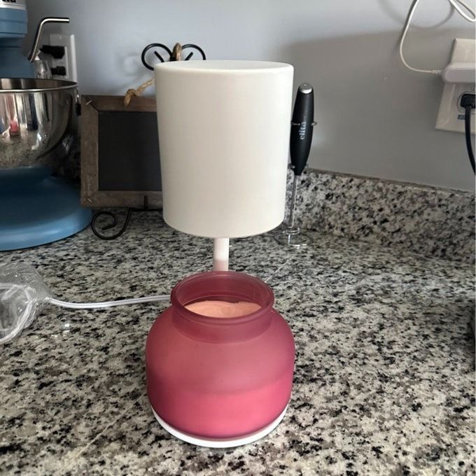 A candle warmer with a pink candle jar sits on a kitchen countertop next to various appliances
