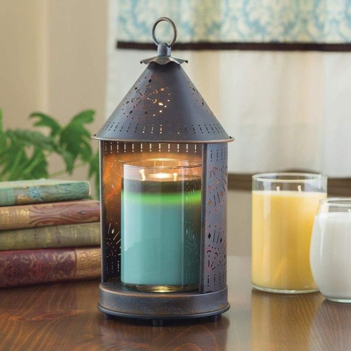 A hut-shaped candle warmer sitting on a table with a candle inside