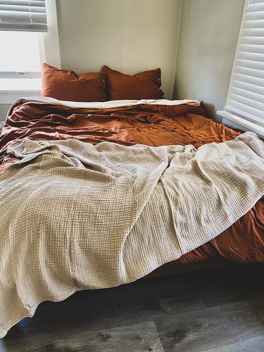 The muslin throw casually draped across the foot of a bed, adding a touch of warmth and comfort.