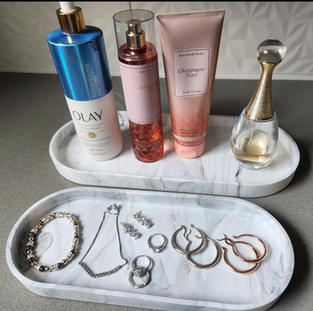 Skincare and fragrance items, such as Olay, Bath & Body Works Champagne Toast, Dior, along with a collection of rings, bracelets, and earrings, neatly arranged on stylish trays.