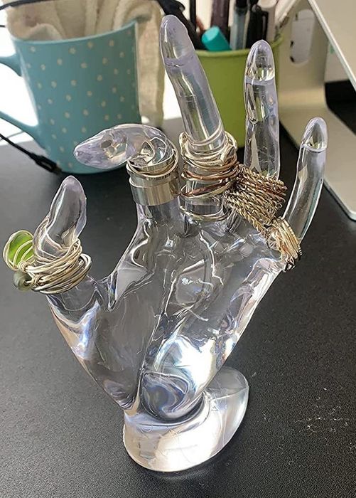 A reviewer's clear plastic hand is shown holding jewelry.