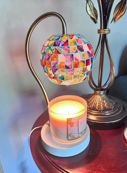 A decorative mosaic lamp with a lit candle on a wooden table, setting a cozy ambiance