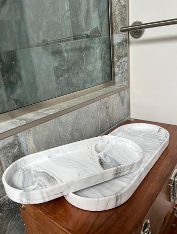 Two oval-shaped marble trays stacked on a wooden surface near a glass shower door, creating a sleek and modern display.
