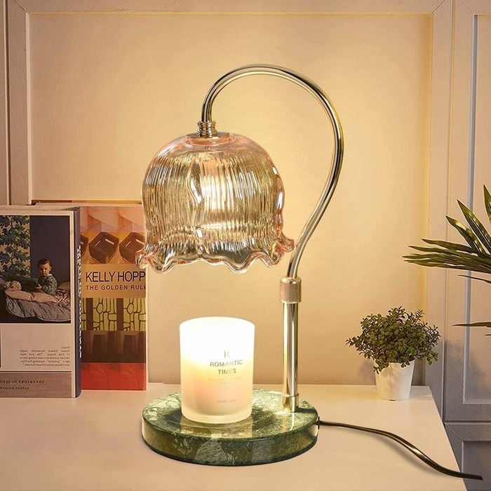 A fashionable lamp with a fluted glass shade, lighting up a desk adorned with a candle, books, and a small plant, creating a warm and inviting ambiance