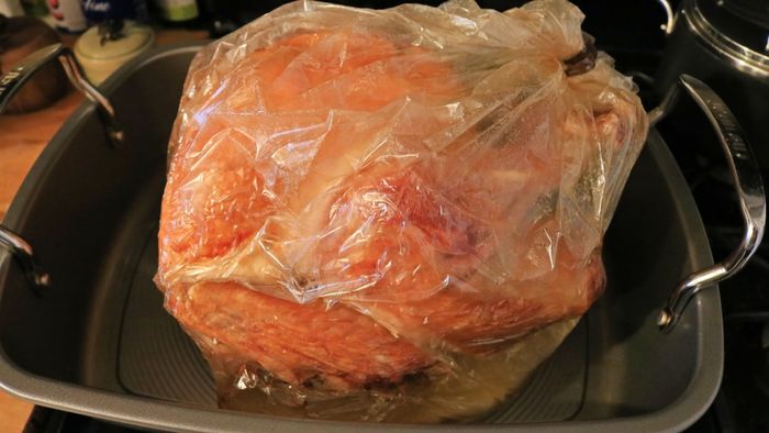 A turkey placed inside a roasting bag within a roasting pan.