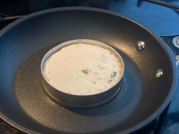 Batter placed inside a metal ring on a frying pan.