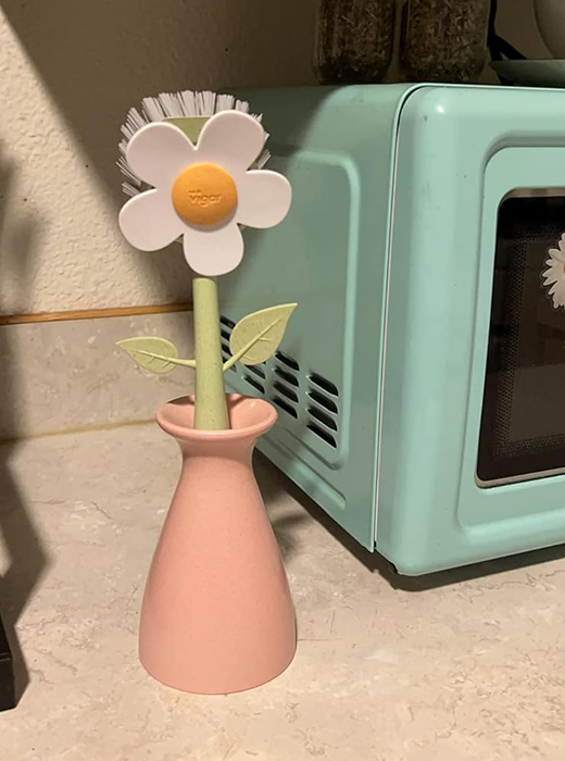 A white daisy-shaped scrubber resting in a pink vase, with its stem standing tall.