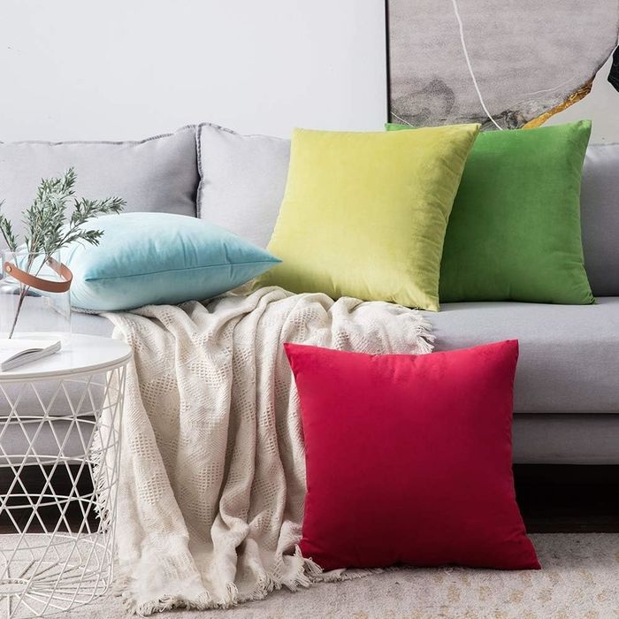 Four velvet throw pillows in shades of light blue, light green, moss green, and red.