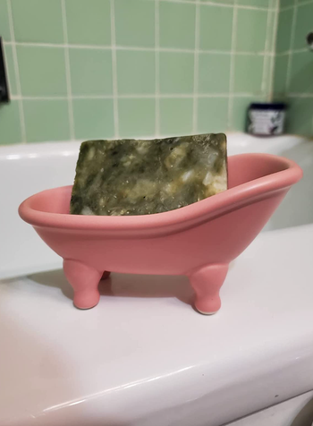 A pink ceramic bathtub cradling a green bar of soap inside.