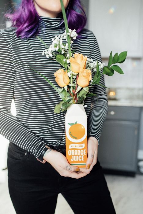 A reviewer holding up the charming orange juice carton vase.
