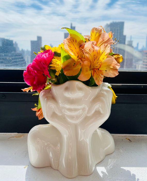 A white vase featuring the bottom half of a face, its head cradled in its hands.