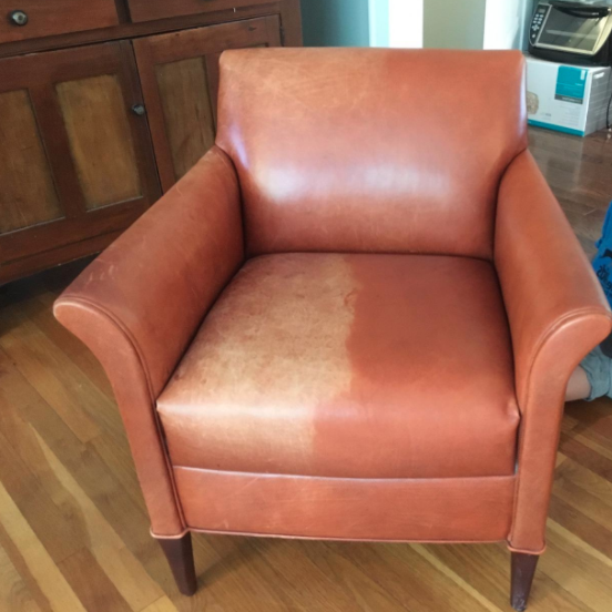 A reviewer’s chair in the process of being restored; one side is faded to a very light brown, while the recolored side has taken on a warm, reddish-brown hue.
