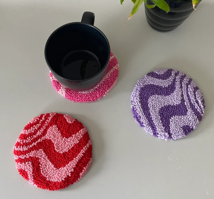 The round wavy coasters in different colors, with one holding a mug.
