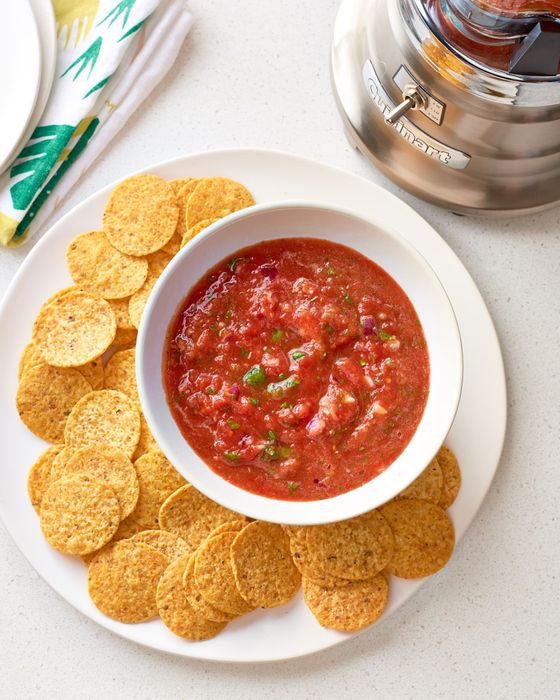 A bowl of salsa placed next to a blender