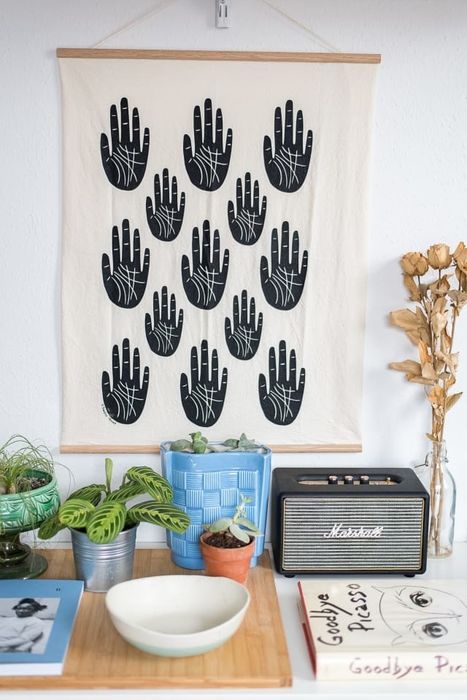 A tea towel with slender wood slats on the top and bottom edges, and a twine loop on the top slat for hanging.