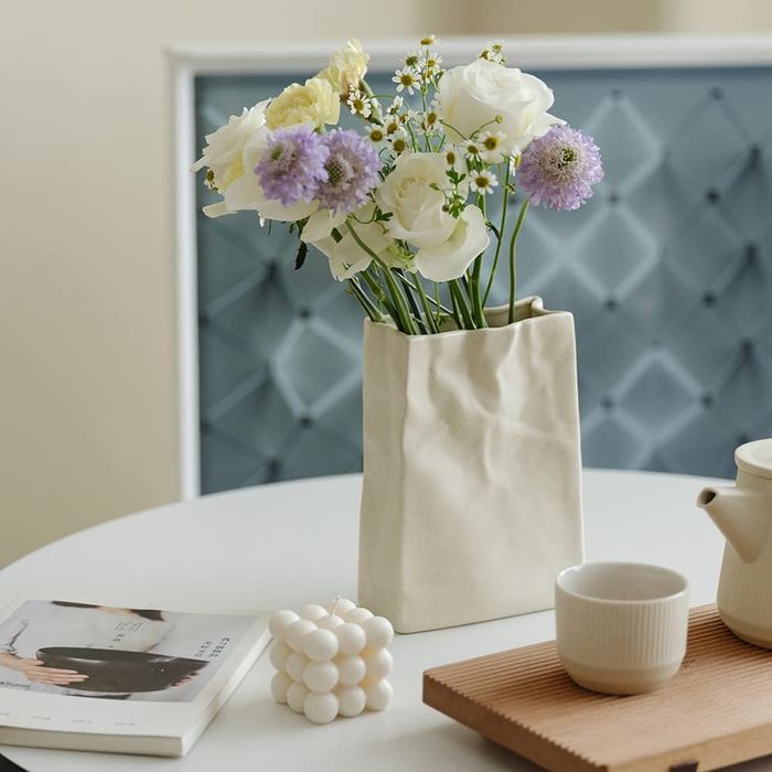 A crumpled, off-white paper bag shaped vase with fresh flowers arranged inside.