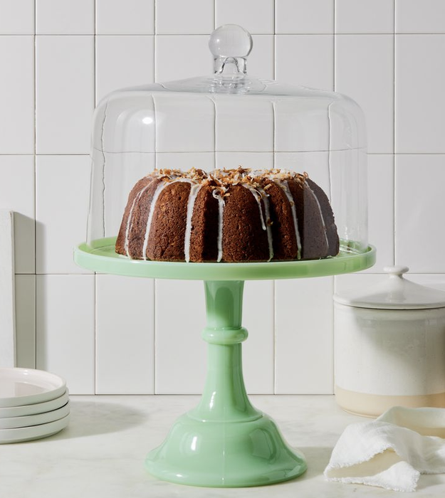 The green cake stand holding a cake, covered by a glass dome