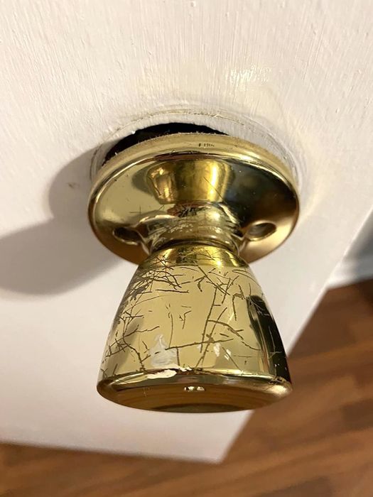 A reviewer's doorknob before, showing the scratched and worn-out old brass finish.